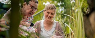 Eine Bewohnerin und eine Mitarbeiterin sind im Garten und betrachten, was dort wächst.