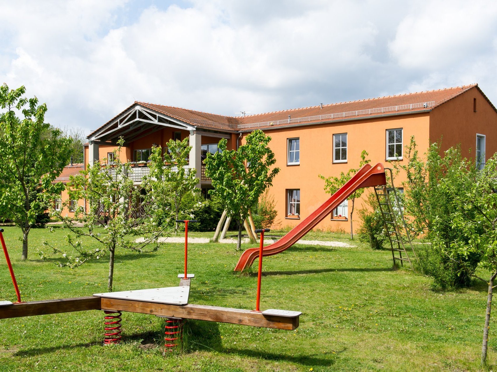 Aussenansicht auf Gebäude mit Garten und Spielplatz