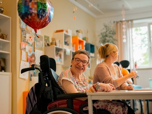 Eine Gruppe von Menschen mit und ohne Beeinträchtigung sitzen am Tisch und unterhalten sich miteinander, während sie gemeinsam Spiele spielen oder an kreativen Projekten arbeiten.