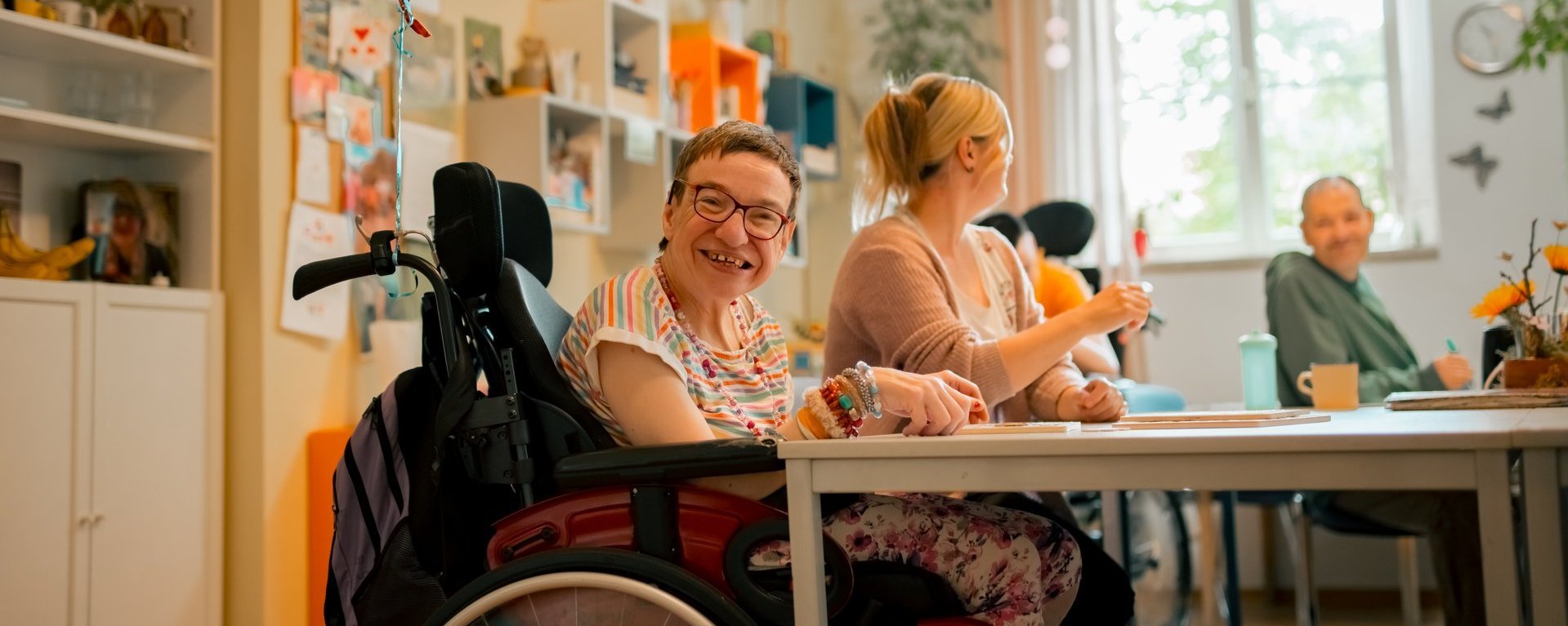 Eine Gruppe von Menschen mit und ohne Beeinträchtigung sitzen am Tisch und unterhalten sich miteinander, während sie gemeinsam Spiele spielen oder an kreativen Projekten arbeiten.