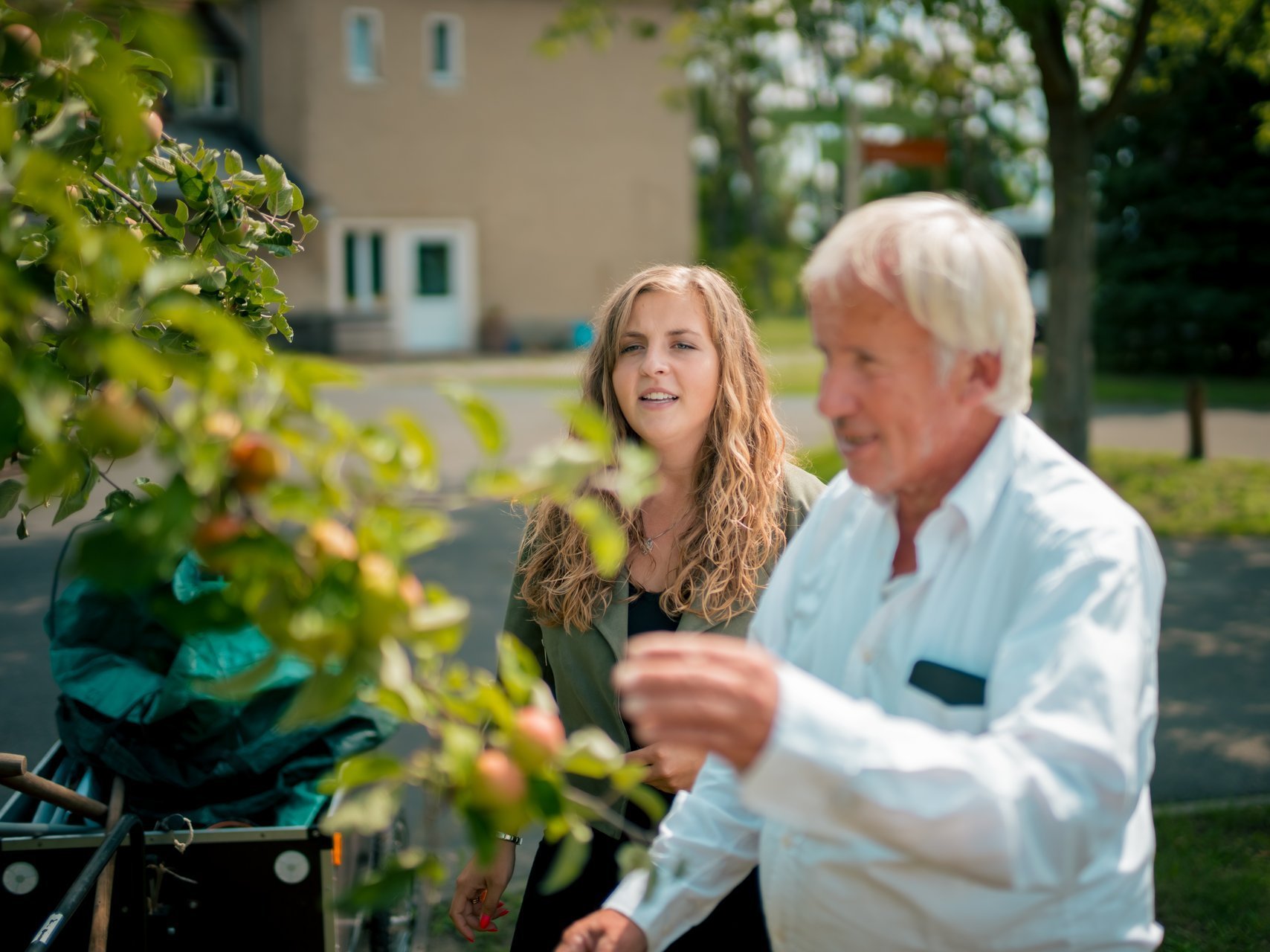 Zwei Mitarbeitende stehen im Garten des Hauses und begutachten die Obstbäume.
