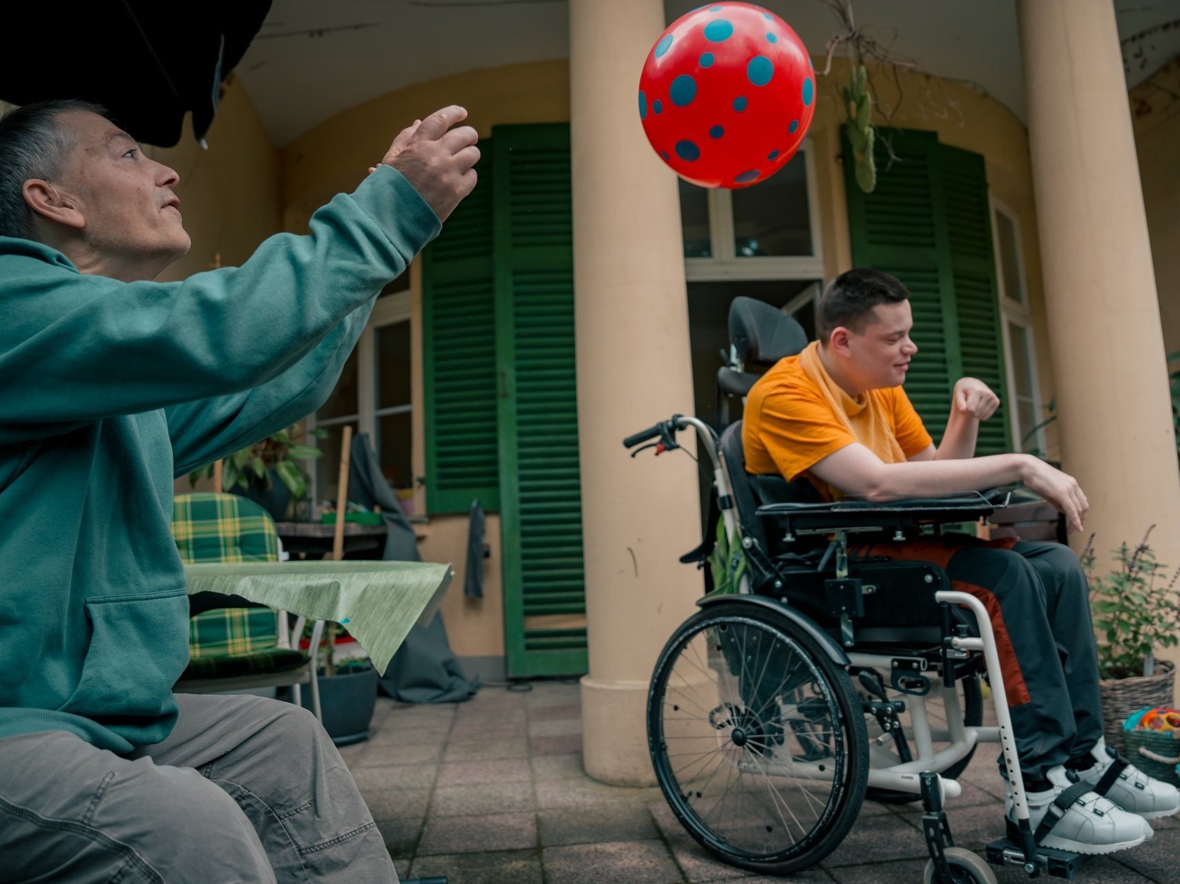 Zwei Bewohner mit Beeinträchtigung werfen sich einen Ball zu und haben dabei sichtbar Spaß.