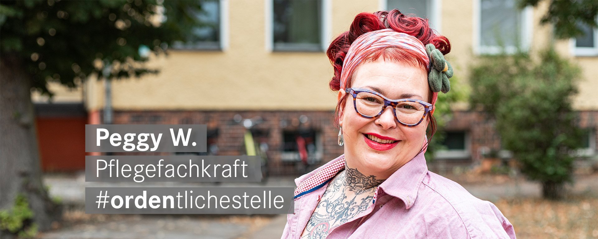 Pflegefachkraft mit roten Haaren Brille und Tattoos laechelt freundlich in die Kamera