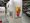 Abstrakte Kunstwerke hängen an weißen Wänden in einer Ausstellungshalle. Ein großes, farbenfrohes Gemälde mit orangen und roten Farbtupfern dominiert den Vordergrund rechts. Daneben sind kleinere Bilder zu sehen. Der Boden ist mit einer Schutzfolie abgedeckt, was auf eine Messe hindeutet.