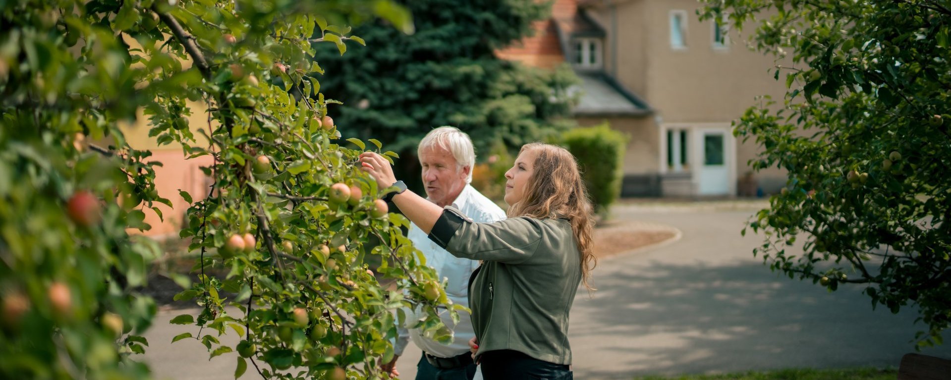 Zwei Mitarbeitende stehen im grünen Garten des Hauses und betrachten die Obstbäume.