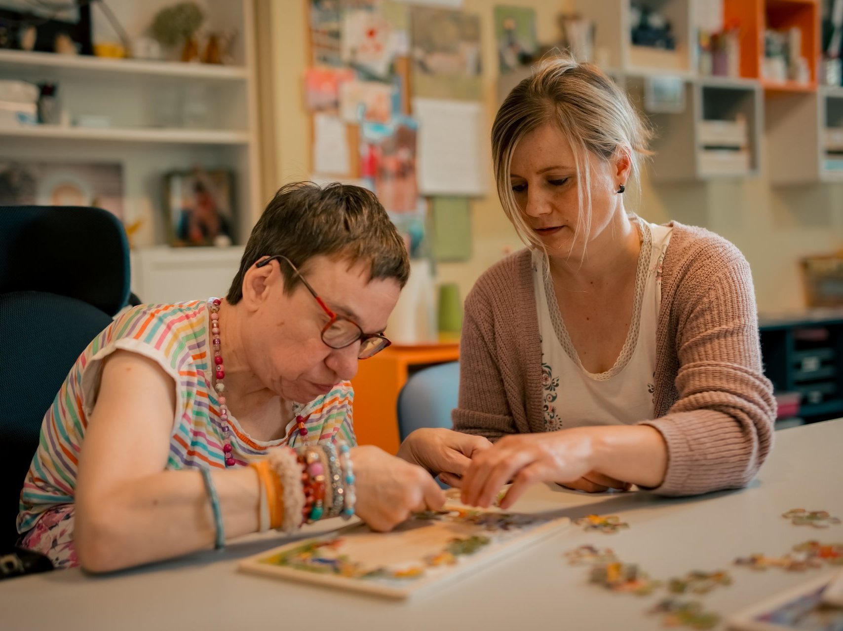 Eine Mitarbeiterin und eine Bewohnerin mit Beeinträchtigung sitzen konzentriert am Tisch und setzen gemeinsam ein Puzzle zusammen.