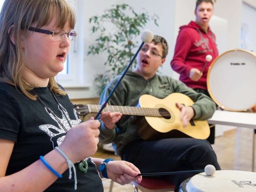 Musikzimmer: en Mädchen und zwei Jungen spielen Trommel und Gitarre