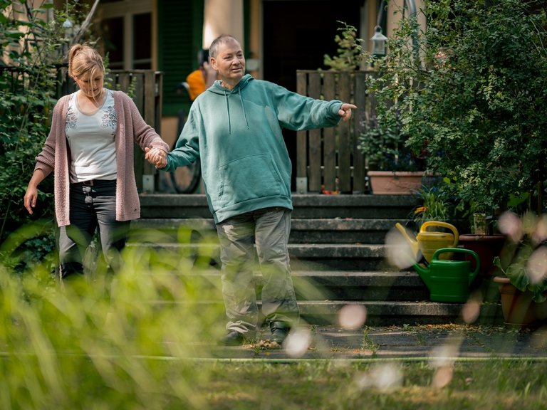 Hand in Hand erkunden ein Bewohner mit Beeinträchtigung und eine Mitarbeiterin den sonnigen Garten.