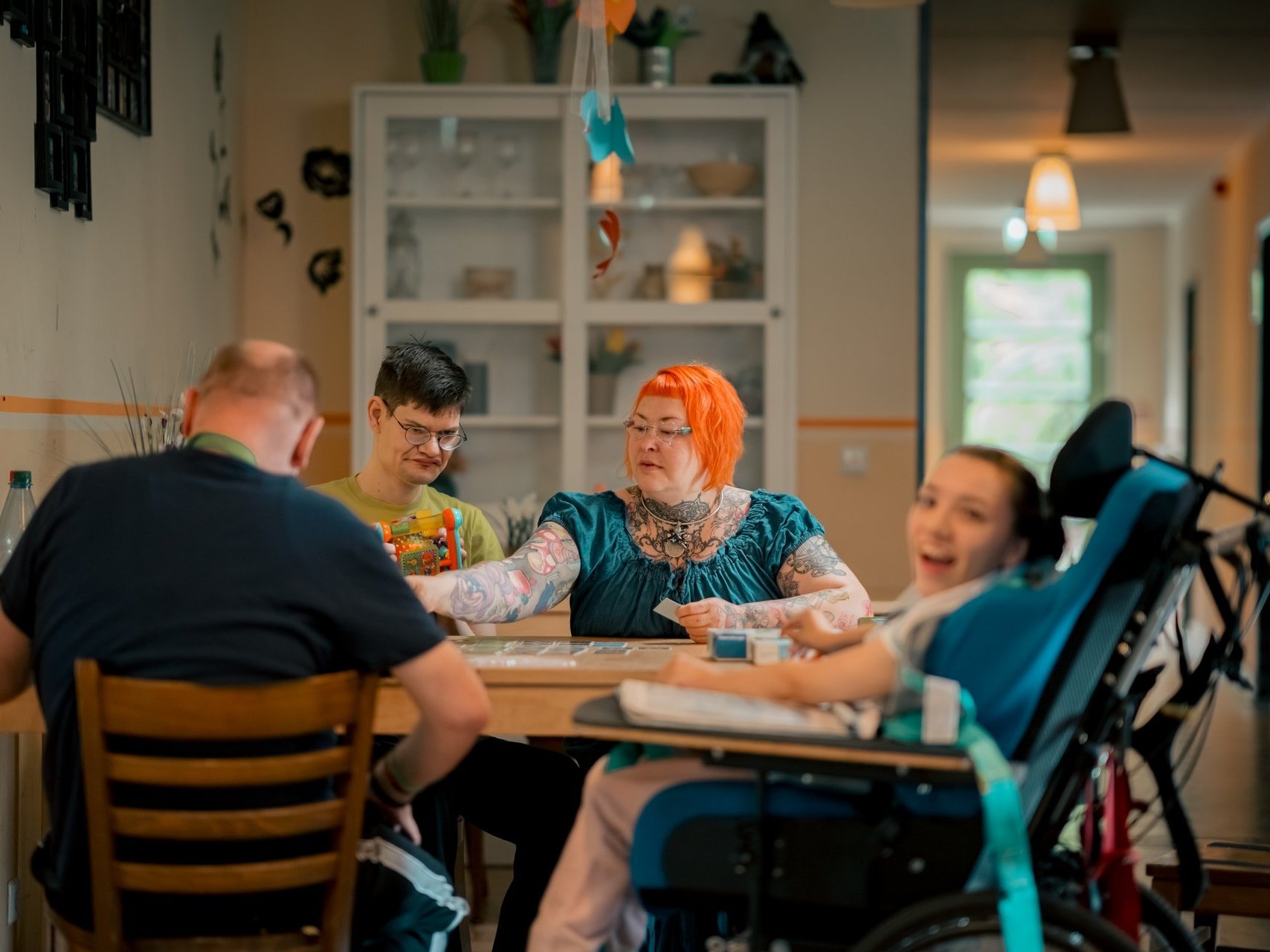 Eine Gruppe von Menschen mit und ohne Beeinträchtigungen sitzt am Tisch. Einige lachen, andere sind vertieft in ihre Beschäftigung.